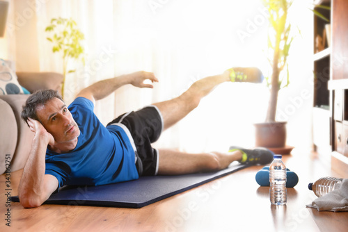 Man doing leg exercises lying on mat in living room