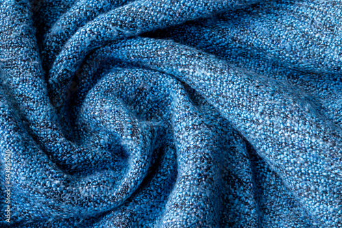 Bright blue knitted fabric texture. Crumpled twisted blanket background. Selective focus. Closeup view