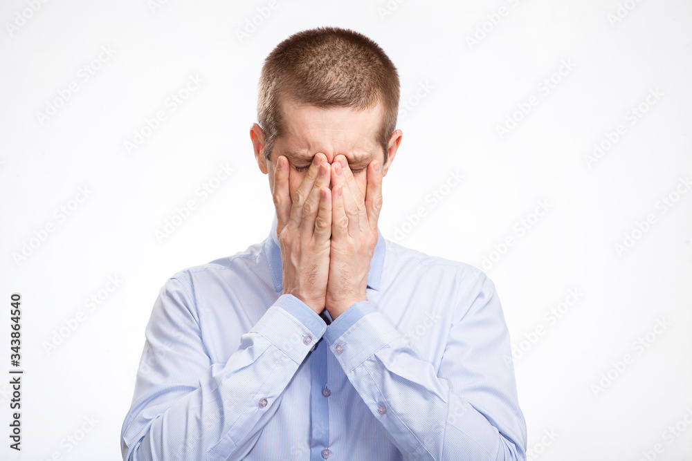 The grieving sad man covered his face and eyes with his hands, experiencing loss and fatigue, in a blue light shirt. Isolated The grieving sad man covered his face and eyes with his hands, experiencing loss and fatigue, in a blue light shirt. Isolated