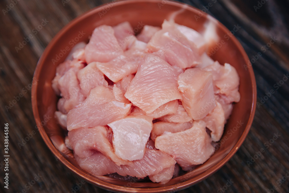 Ingredient for cooking. Raw turkey diced in a black cup on a dark kitchen table. Fillet cut into pieces. Chicken meat Ingredient for cooking. Raw turkey diced in a black cup on a dark kitchen table. Fillet cut into pieces. Chicken meat