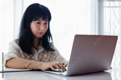 Asian woman using laptop and working at home for business, self-quarantine, staying home and social distancing in coronavirus or Covid-2019 outbreak situation concept © Kesinee