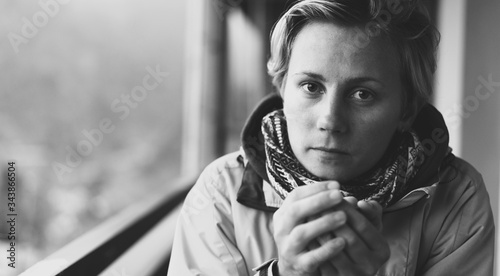 A young beautiful caucasian adult girl is sitting and drinking tea after a long trek, black and white, kind look
