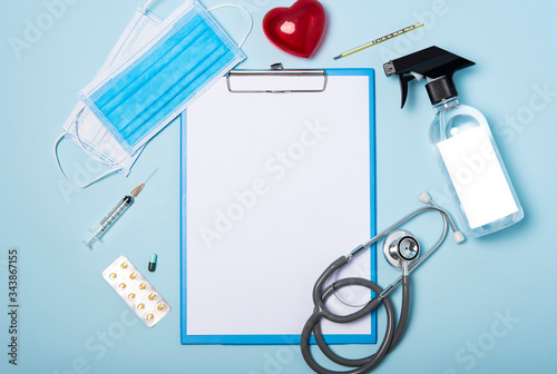 medical equipment mockup clipboard, stethoscope with red heart and drug, surgical mask on blue copy space background.