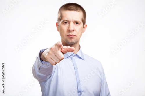 successful business man points his index finger at the camera, in a blue light casual shirt, looking at the camera. Isolated