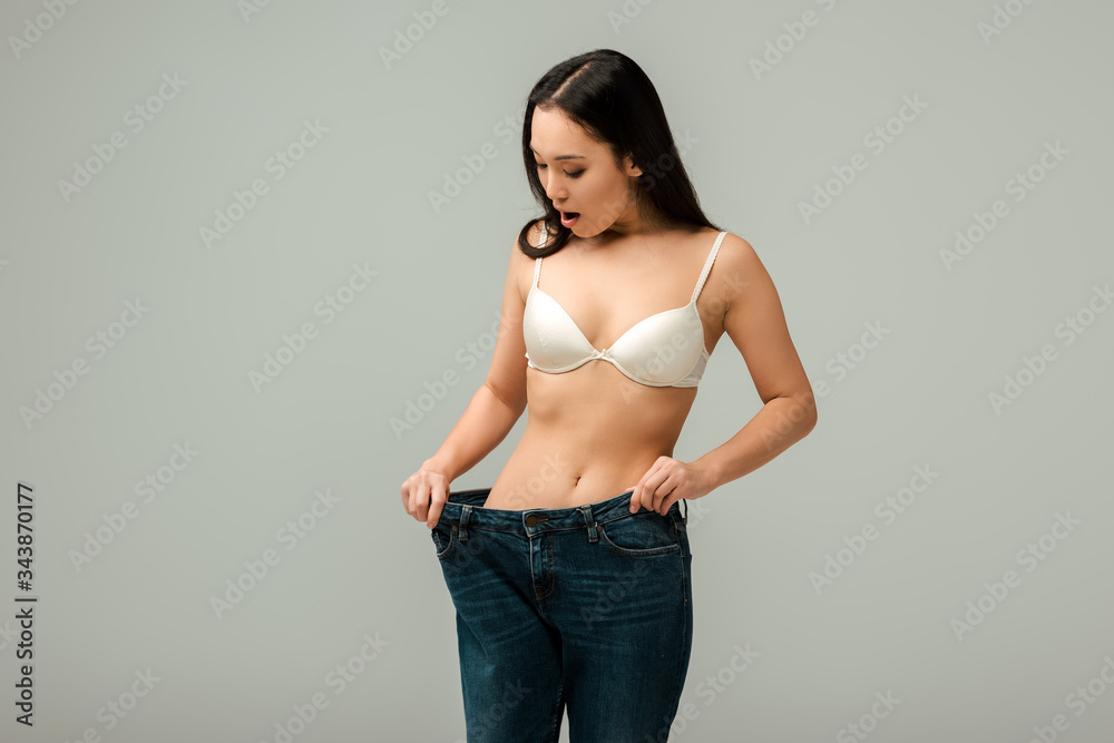surprised asian girl touching oversized jeans isolated on grey surprised asian girl touching oversized jeans isolated on grey