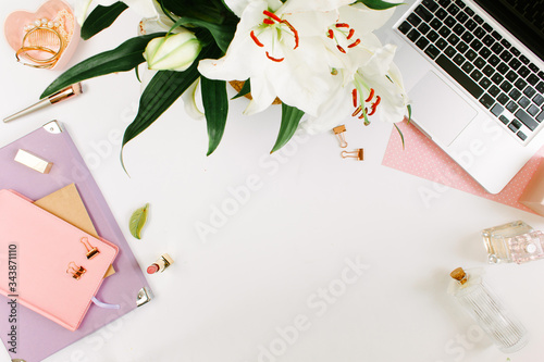 Creative colorful female workspace with laptop computer, flowers, colorgul notebooks, golden clips on white desk. Flat lay, top view photo