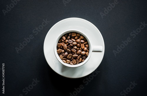 Top view of roasted coffee beans in white coffee cup with black background 