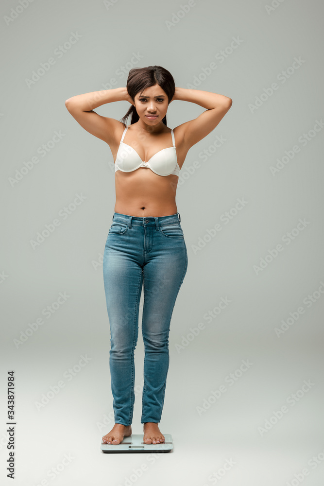 overweight african american woman in jeans and bra standing on scales and touching hair on grey overweight african american woman in jeans and bra standing on scales and touching hair on grey