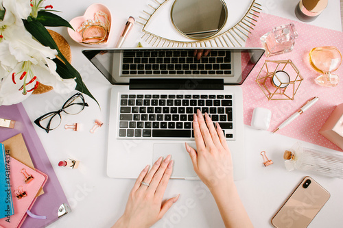 Woman work on laptop. Creative desk workspace with computer, clips, flowers, cosmetics, glasses. Flat lay style. Freelance and remote work concept