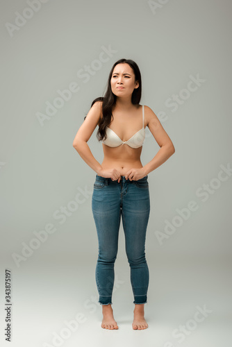 displeased and overweight asian girl wearing jeans on grey