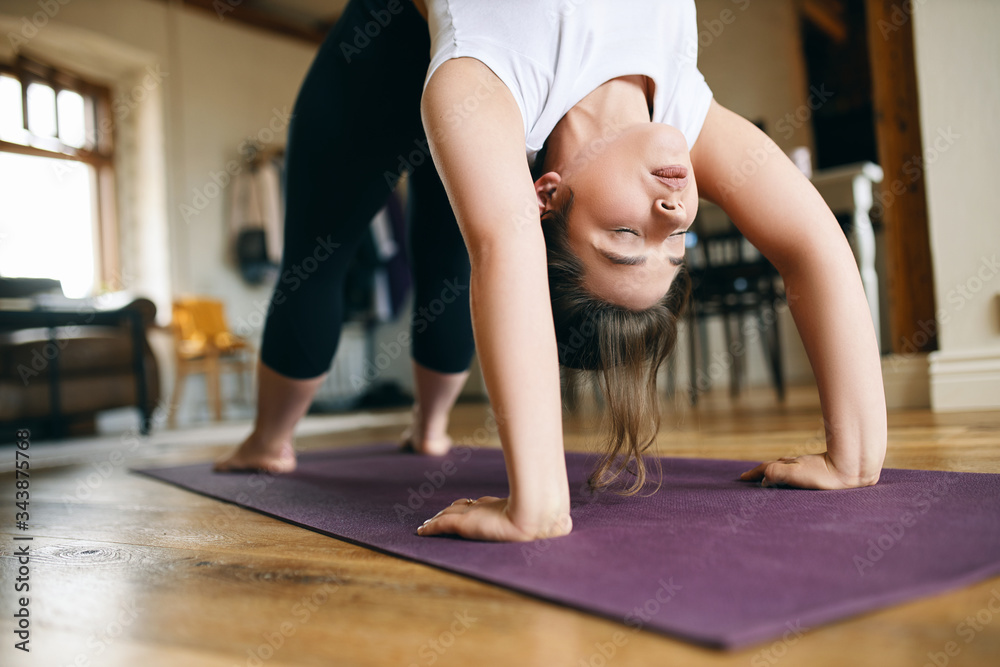 Close up image of young female yogi practicing advanced yoga at home, doing upward bow or wheel pose, backbending, keeping hands and feet on mat, stretching spine and opening chest. Health and energy Close up image of young female yogi practicing advanced yoga at home, doing upward bow or wheel pose, backbending, keeping hands and feet on mat, stretching spine and opening chest. Health and energy