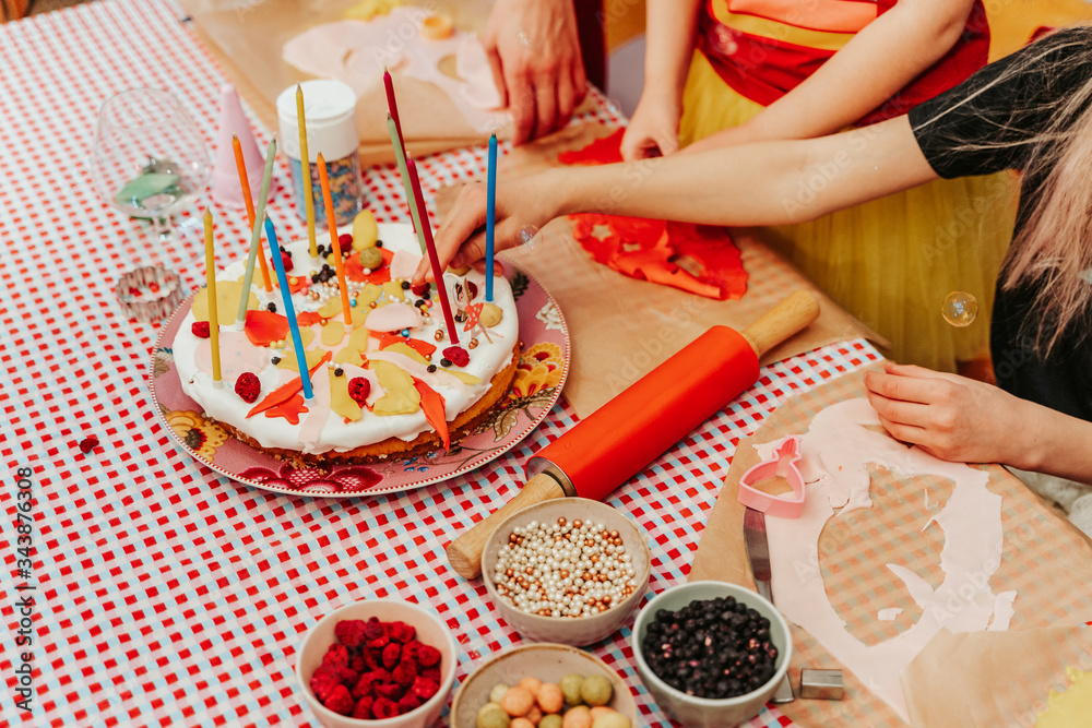 Fototapeta premium Children preparing homemade birthday cake with candles and colorful topping.