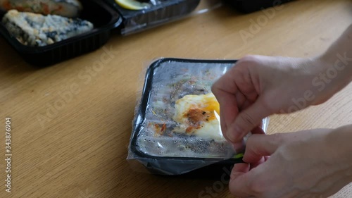 Food delivery concept: woman opening plastic box with japanese food, close up. Take away hot food