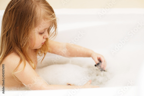 little baby girl with blond hair playing with foam in a bath tub. girl takes a bath. girl playing with toys in the bath