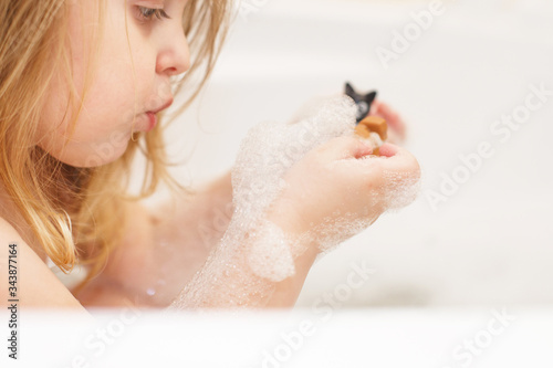 little baby girl with blond hair playing with foam in a bath tub. girl takes a bath. girl playing with toys in the bath