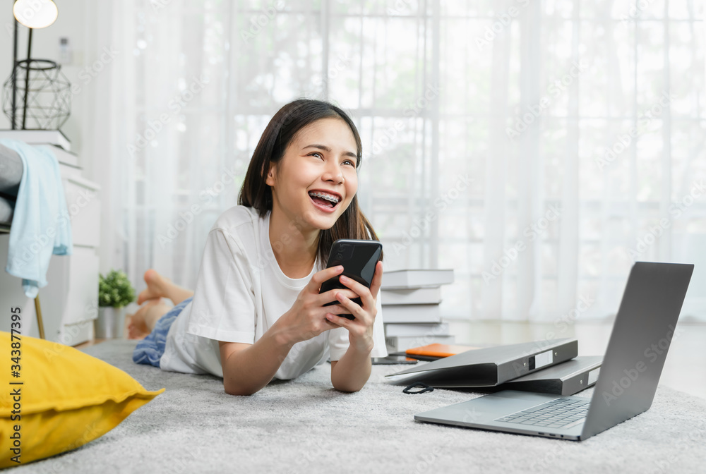 Cheerful beautiful Asian woman holding a smartphone with laptop and using online social media on lifestyle in house. Technology for communication concept. Cheerful beautiful Asian woman holding a smartphone with laptop and using online social media on lifestyle in house. Technology for communication concept.