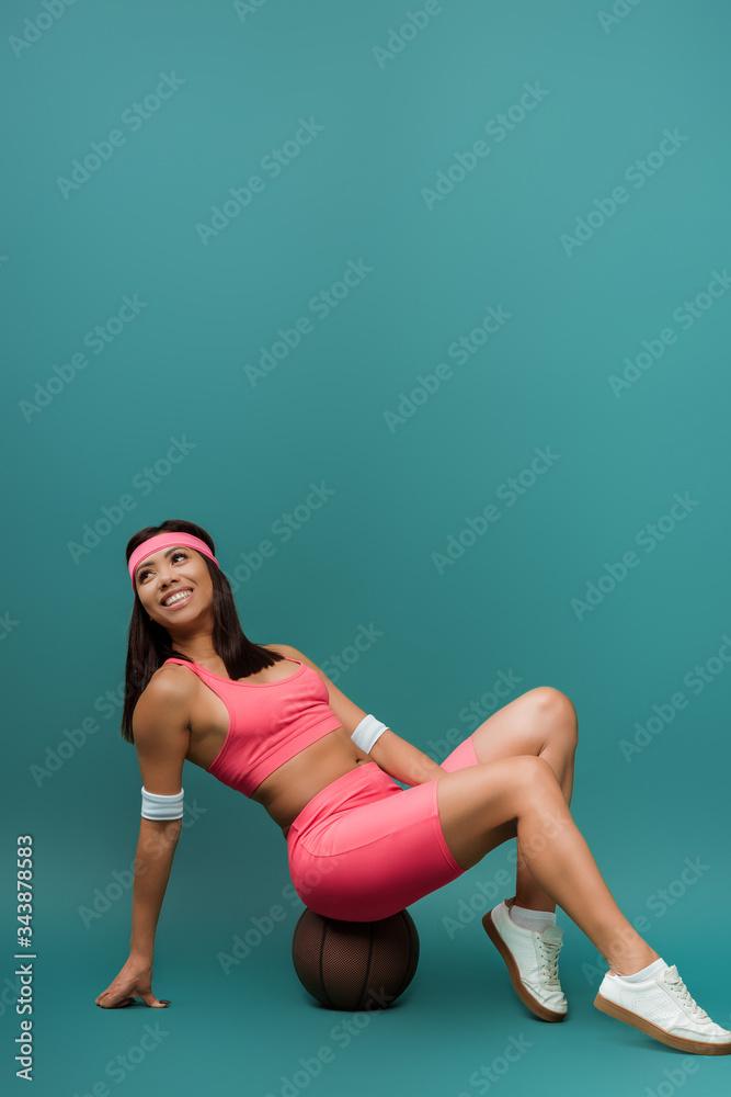 Happy african american sportswoman sitting on ball and smiling on green background