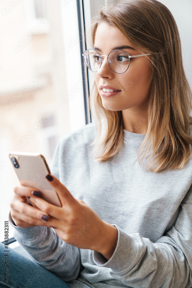 Photo of serious woman using smartphone while sitting near window Photo of serious woman using smartphone while sitting near window
