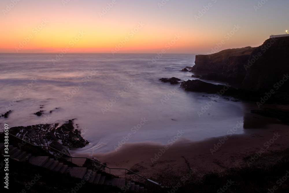 Beach Praia da Zambujeira do Mar at sunset, cliff rocks and waves in motion. Solo Backpacker Trekking on the Rota Vicentina and Fishermen's Trail in Alentejo, Portugal. Walking between cliff, ocean, n