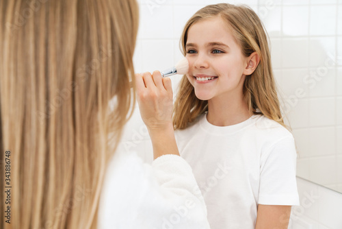 Photo of mother and daughter smiling while doing makeup in bathroom