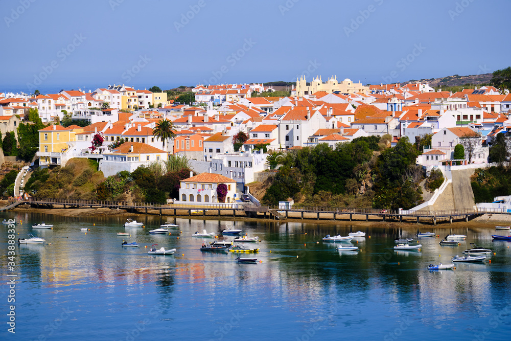 The city Vila Nova de Milfontes is reflected in the waters of the harbor full of boats. Solo Backpacker Trekking on the Rota Vicentina and Fishermen's Trail in Alentejo, Portugal. Walking between clif