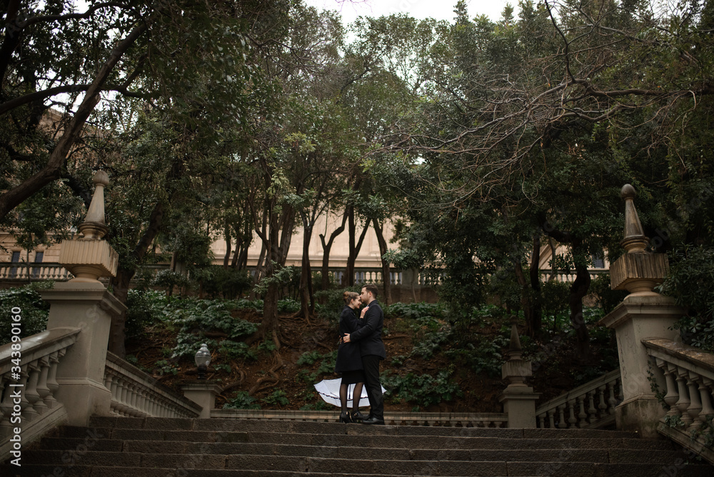 Young beautiful loving Hispanic couple walks under an umbrella during the rain in Plaza Spain. Couple posing against the backdrop of the National Museum of Art of Catalonia.