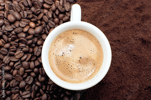 A cup of fresh coffee with foam. Background of coffee beans and ground coffee