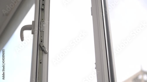A man opens and closes a white plastic window by the handle.