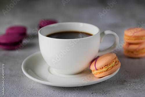 White cup with black coffee and bright macaroon cakes on a concrete background.