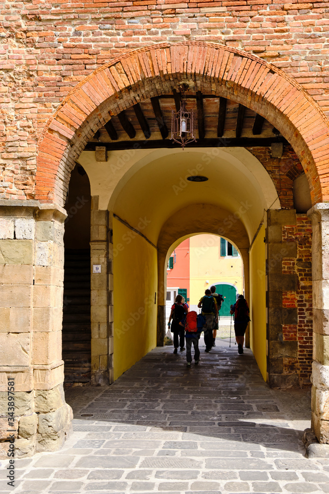 Pilgrims walkings under arcades in little town Porcari. Solo Backpacker Trekking on the Via Francigena from Lucca to Siena. Walking between nature, history, churches,
