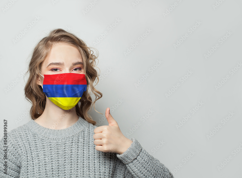 Happy woman in face mask holding thumb up and Armenian flag background. Flu epidemic and virus protection concept Happy woman in face mask holding thumb up and Armenian flag background. Flu epidemic and virus protection concept