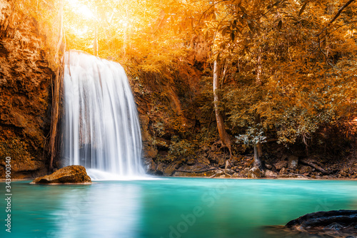 Waterfall and blue emerald water in autumn forest with sun flare and sunlight in morning. Erawan Waterfall step 3rd. Beautiful nature rock waterfall steps in rainforest at Kanchanaburi, Thailand