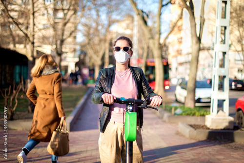 Young woman wearing face mask and riding electric scooter during coronavirus pandemic in the city