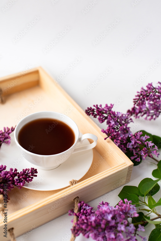 porcelain cup with coffee, cocoa, spring breakfast on a wooden tray. Branches and flowers of lilac, violet color, on a white background. Minimalistic design porcelain cup with coffee, cocoa, spring breakfast on a wooden tray. Branches and flowers of lilac, violet color, on a white background. Minimalistic design
