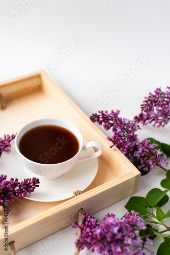  porcelain cup with coffee, cocoa, spring breakfast on a wooden tray. Branches and flowers of lilac, violet color, on a white background. Minimalistic design