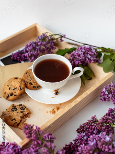 Cup with coffee, cocoa, chocolate chip cookies, spring breakfast on a wooden tray. Lilac branches, a bouquet of purple color, on a white background. Minimalistic design, top view, creative flat lay
