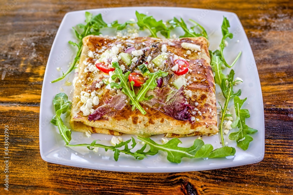 Greek salad crepe sandwich with arugula, tomatoes, cucumber, and feta cheese on white decorated plate. Greek salad crepe sandwich with arugula, tomatoes, cucumber, and feta cheese on white decorated plate.