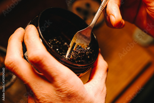 Φωτογραφία Hookah-maker is preparing moist fruit tobacco with fork, placing it in a bulb sh