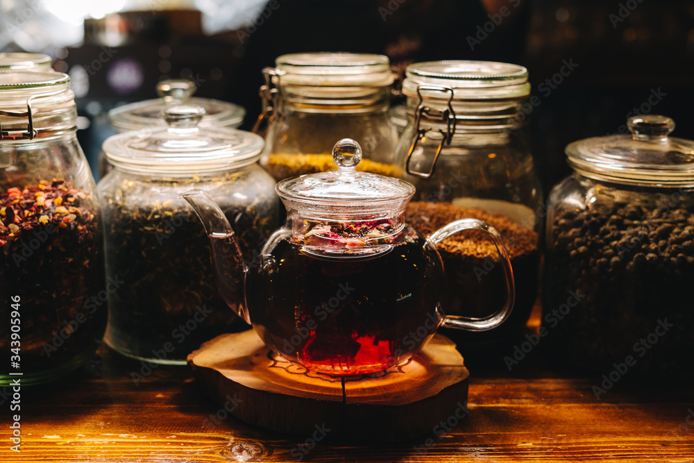 A teapot of black tea standing in front of jars filled with tea leaves, warm light, close up A teapot of black tea standing in front of jars filled with tea leaves, warm light, close up