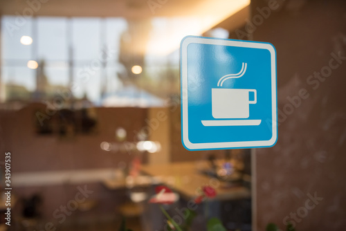 Close up to sticker of symbol coffee shop on glass background. Cafe wallpaper view. sticker on the window with a picture of a cup of coffee. coffee bar sticker on a glass blue