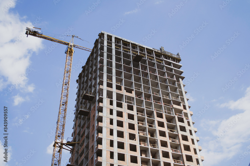 Construction of a multi-storey residential building. Construction crane. Against the blue sky