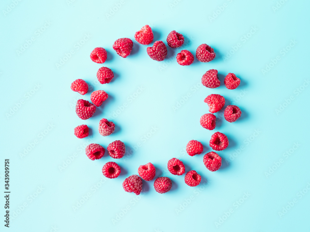 Fototapeta premium Creative layout with fresh ripe berries. Raspberry on blue background with round empty circle in center for copy space. Can use for your design. Top view or flat lay. Negative space for text