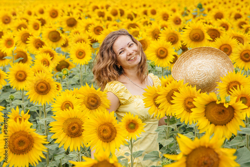 Portrait of a young woman in a straw hat on a field of sunflowers. Natural, imperfect skin.