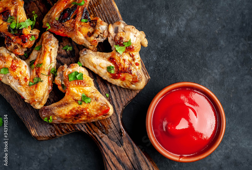 Grilled chicken wings in barbecue sauce on a wooden board on a concrete table with copy space for your text.