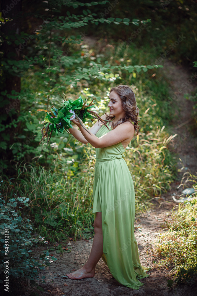 Beautiful young woman in a green dress and a wreath in a sunny forest Beautiful young woman in a green dress and a wreath in a sunny forest