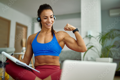 Wallpaper Mural Happy muscular build woman flexing her bicep while using laptop at home