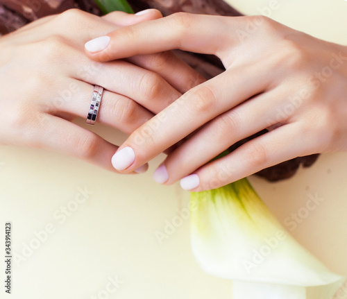 pretty perfect woman hands with white manicure and big flower on colorful yellow background, spa concept