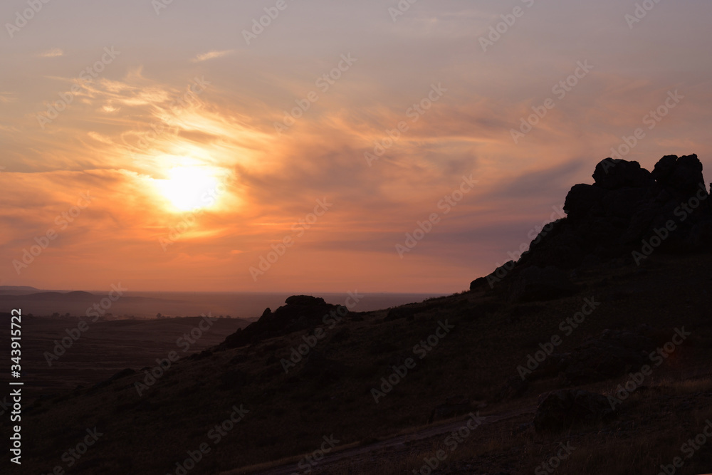 Silhouettes of rocks on a sunset background over a plain