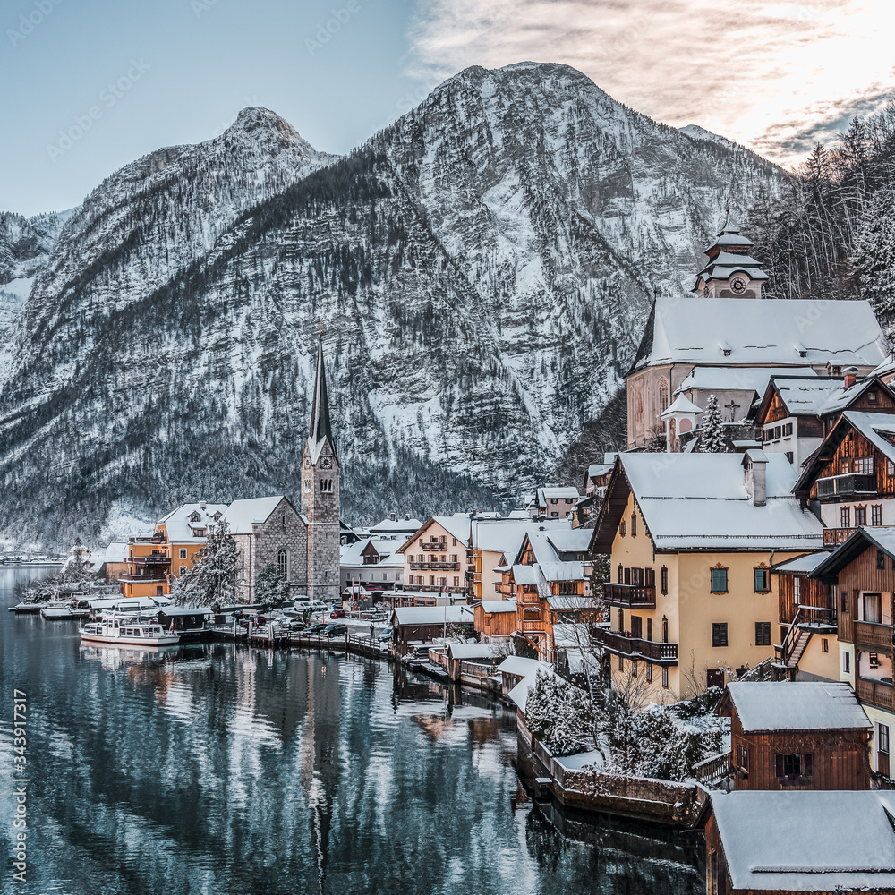 Fototapeta premium Snowy village Hallstatt by lake at foot of snow mountain with clear sky in winter in Austria
