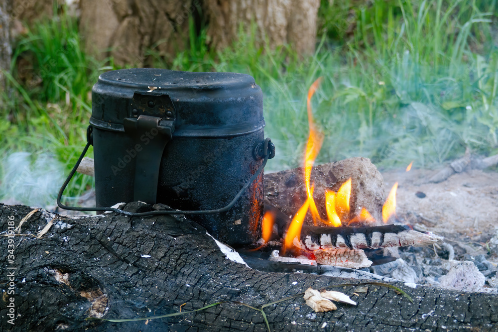 Old black military bowler in campfire, hiking smoked pot on the coals in summer evening. Selective focus. Old black military bowler in campfire, hiking smoked pot on the coals in summer evening. Selective focus.